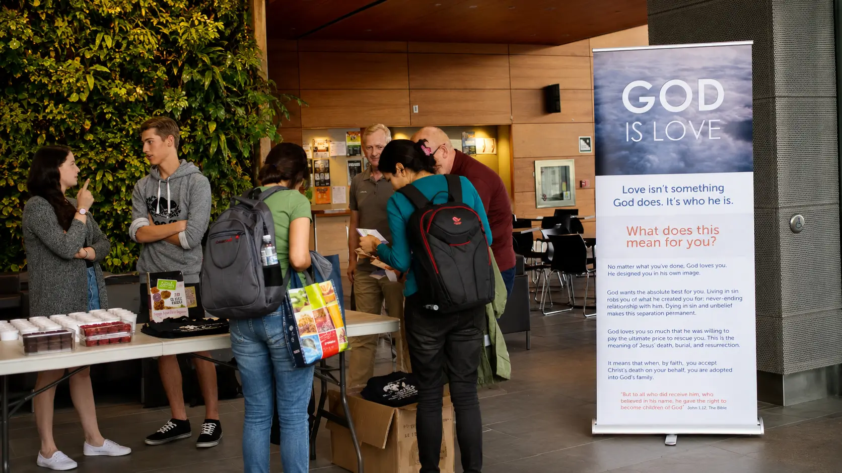 People speaking with University of Ottawa students beside a gospel banner reading “God Is Love”